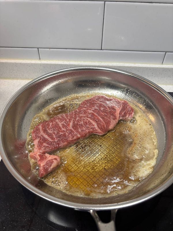 A piece of hanwoo sirloin is sizzling in a frying pan.