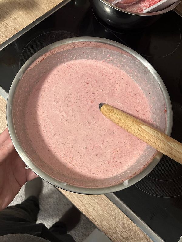 A bowl of homemade strawberry ice cream mixture is being prepared.