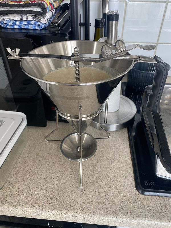 A stack of pancakes topped with butter and syrup on a white plate next to a glass of orange juice on a wooden table.