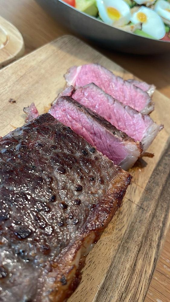 A grilled steak served on a white plate with vegetables and sides on a wooden table.