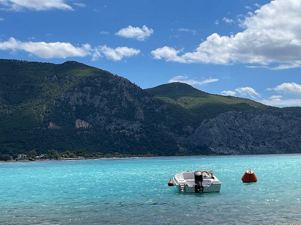 A serene coastal scene featuring a boat anchored in turquoise waters with mountains in the background.