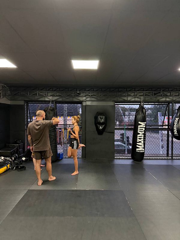 A gym room with a Muay Thai boxing focus, featuring boxing gloves, heavy bags, and a punching ring carpet.