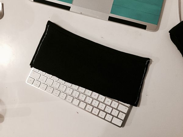 A keyboard partially covered by a black fabric sleeve is placed on a desk.