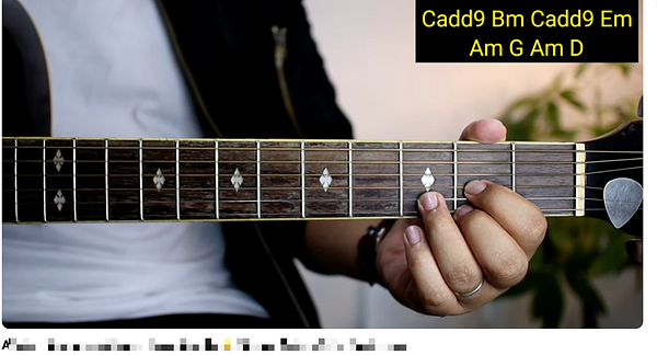 Close-up of a person playing a wooden acoustic guitar, focusing on the fretboard and hand placement.