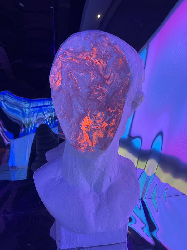 A sculptural bust with a vibrant, glowing design is displayed in a colorful, abstract environment.