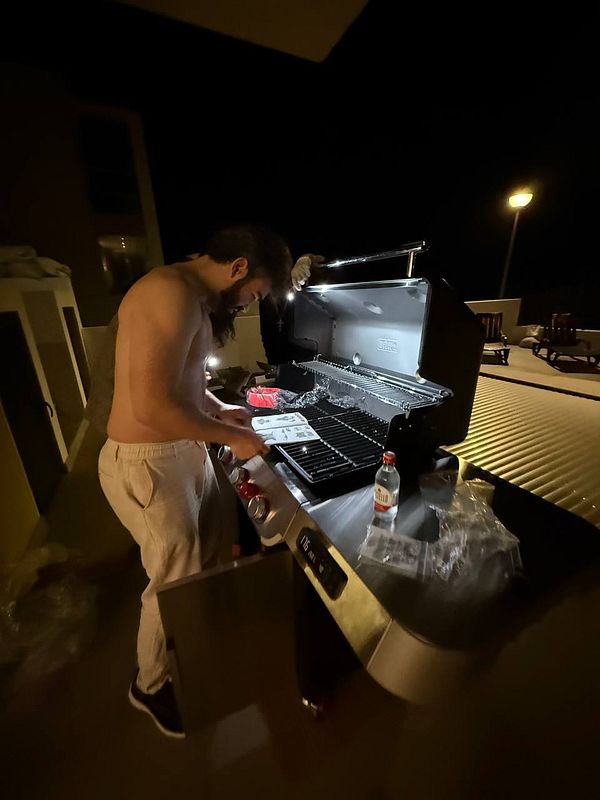 A man is preparing a barbecue at night, focused on the grill.