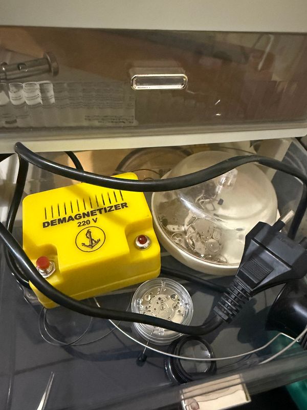 A demagnetizer and various watch components are displayed in a drawer.