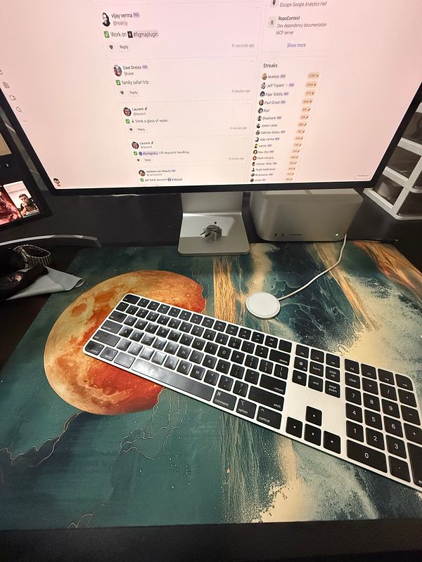 A workspace featuring a colorful desk mat with a cosmic design, a keyboard, and a computer monitor displaying a chat interface.