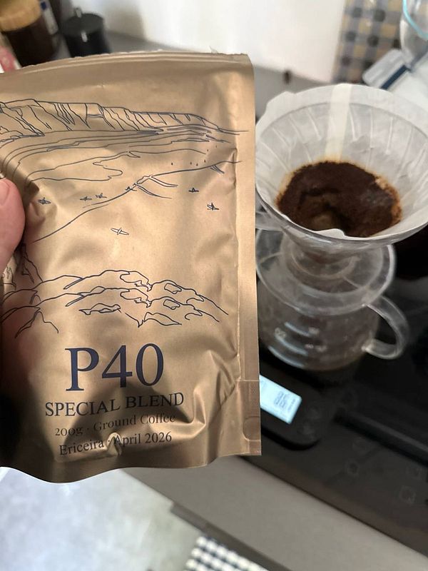 A cup of coffee on a dark textured table with a small spoon and a black object beside it.