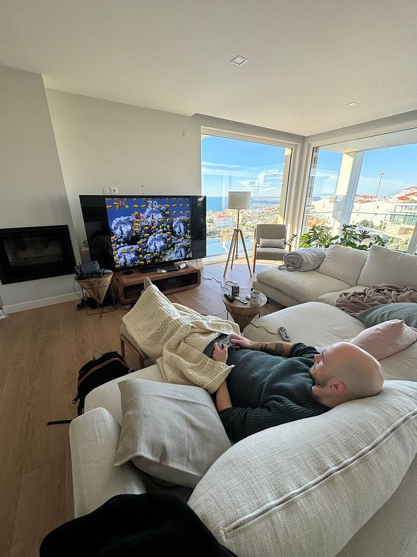 A person is relaxing on a couch in a modern living room while watching a TV screen displaying a colorful image.