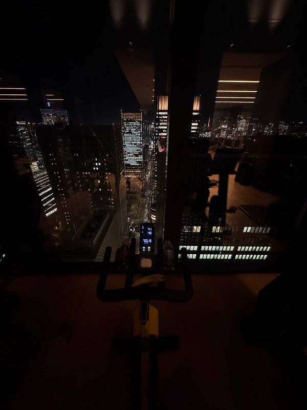A gym setup with a stationary bike overlooks a vibrant Tokyo skyline at night.