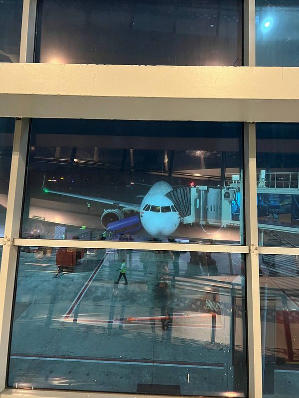 A view of an airplane at an airport terminal through large glass windows.