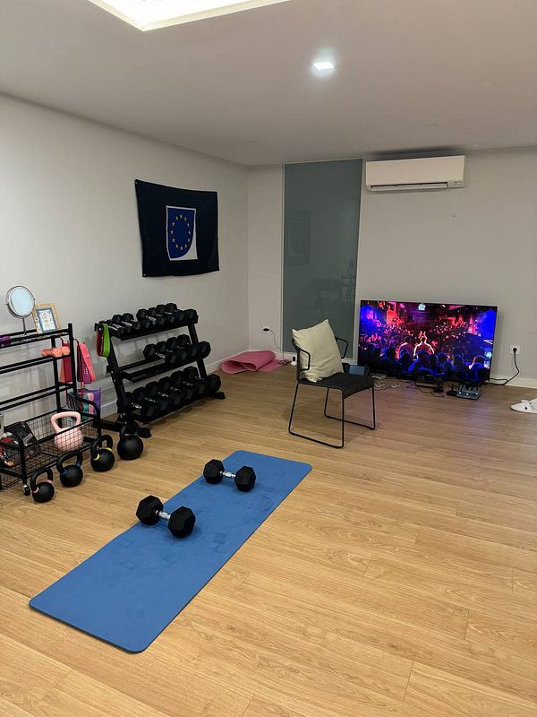 A home gym setup featuring weights, a workout mat, and a television displaying a lively scene.