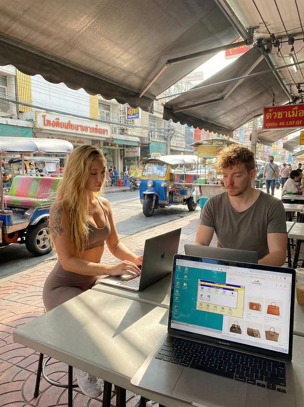 A vibrant outdoor scene featuring two individuals working on laptops at a café in a bustling street.