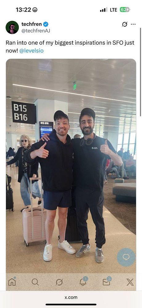 Two men pose together in an airport terminal, smiling and looking happy.