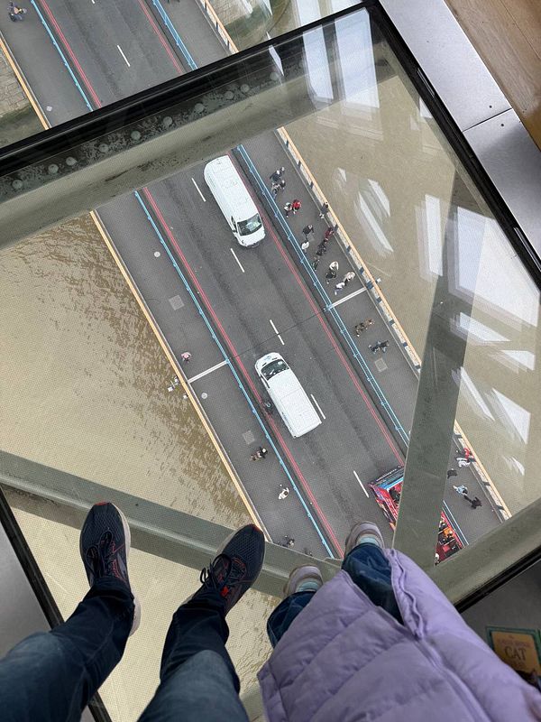 A view from above the London Bridge showing pedestrians and vehicles below through a glass floor.
