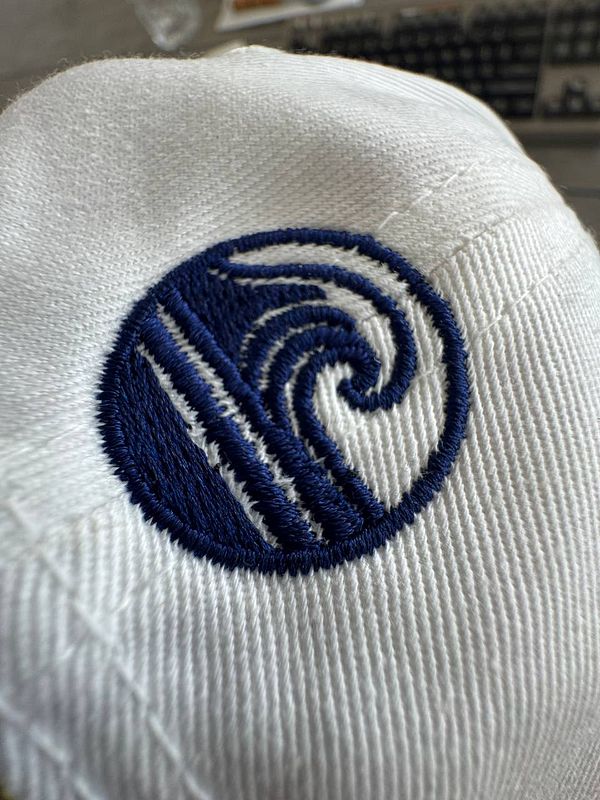 A close-up view of a white hat featuring an embroidered logo.