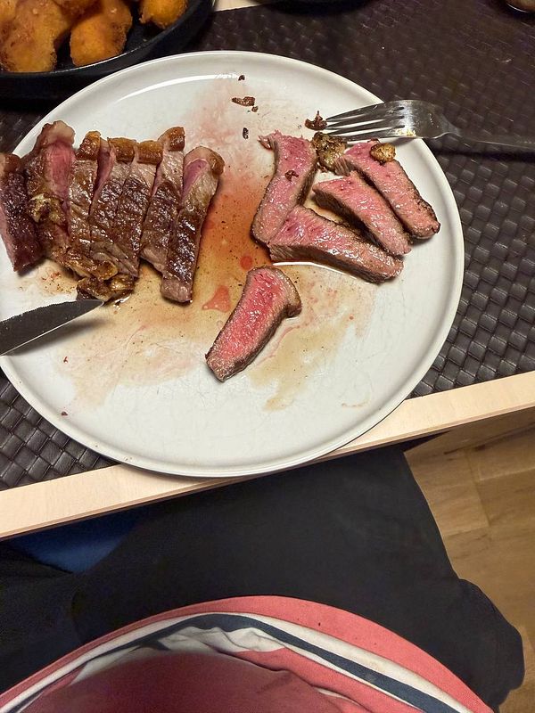 A plate with sliced Picanha steak and a fork, accompanied by a view of a person's lap.