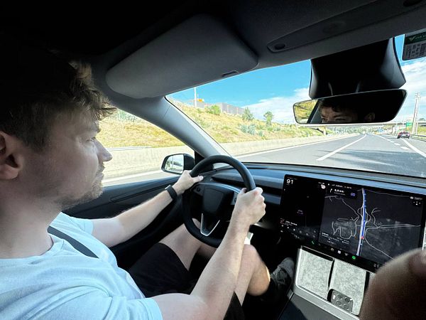 A person is driving a car on a highway, with a focus on the vehicle's dashboard display.