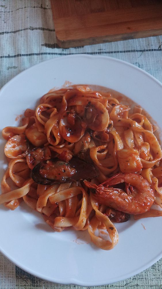 Close-up of a cooked seafood pasta dish in a black pan with lemon wedges.