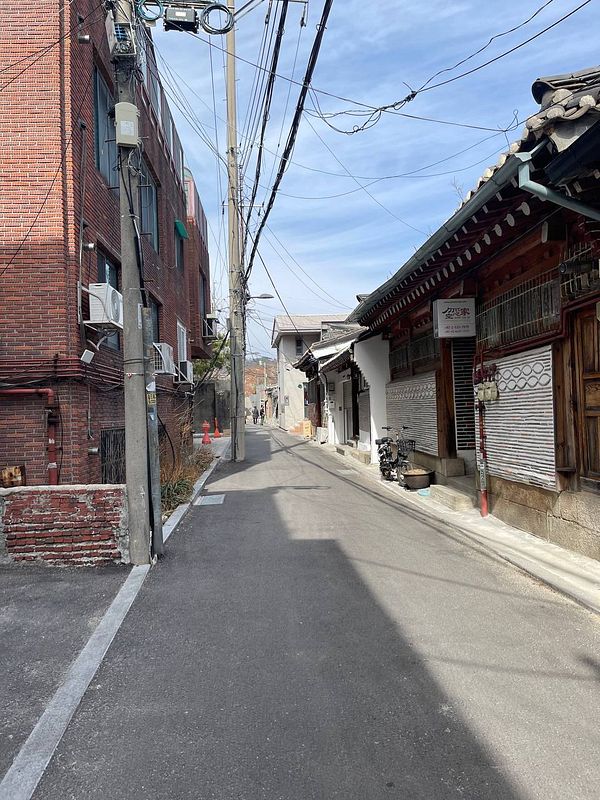 A narrow street in Seoul lined with traditional and modern buildings.