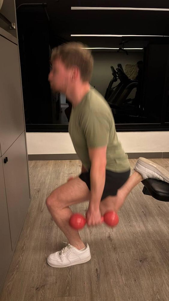 A person is performing a workout in a gym setting, focusing on a squat exercise while holding dumbbells.