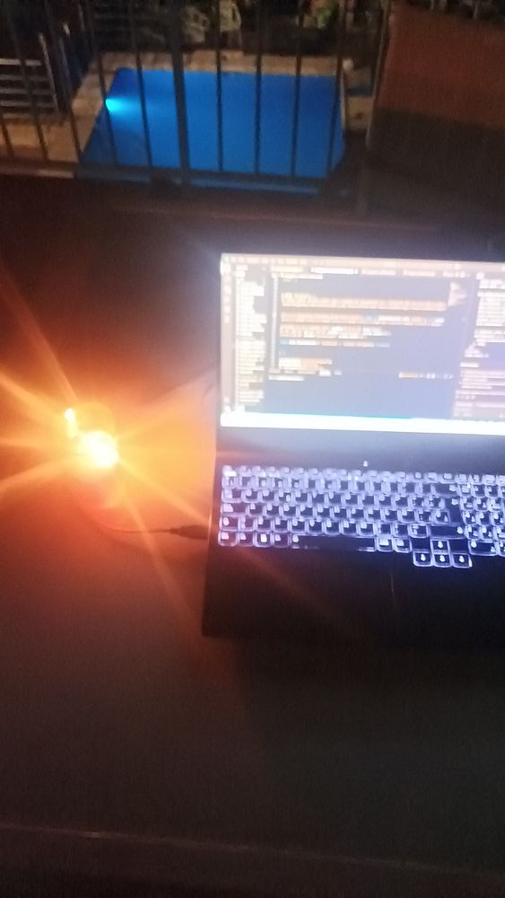A laptop is set up on a terrace at night, illuminated by a candle and with a pool visible in the background.