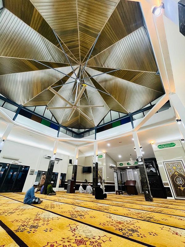 The image captures the interior of a mosque with a unique ceiling design and worshippers engaged in prayer.