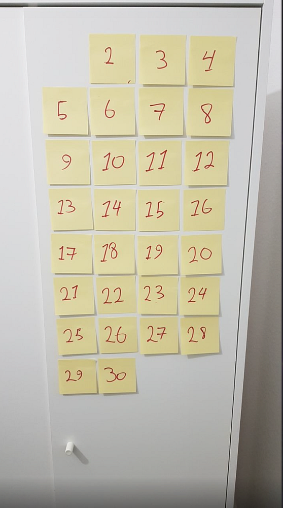A grid of yellow sticky notes displaying numbers from 2 to 30 is arranged on a white surface.