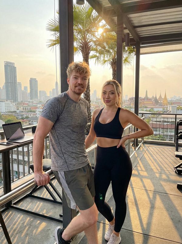 A man and a woman pose together on a rooftop with a city skyline in the background during sunset.