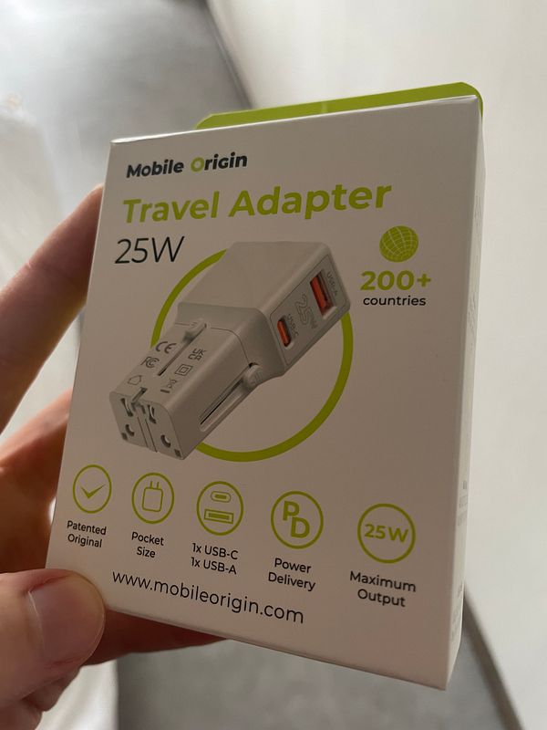 A hand holds a travel adapter box designed for international use.