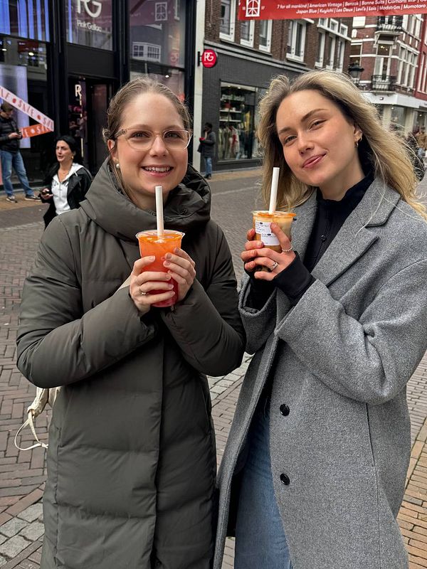A close-up image of a bubble tea cup with a milk tea drink, tapioca pearls at the bottom, and a large bubble tea straw, placed on a white surface.
