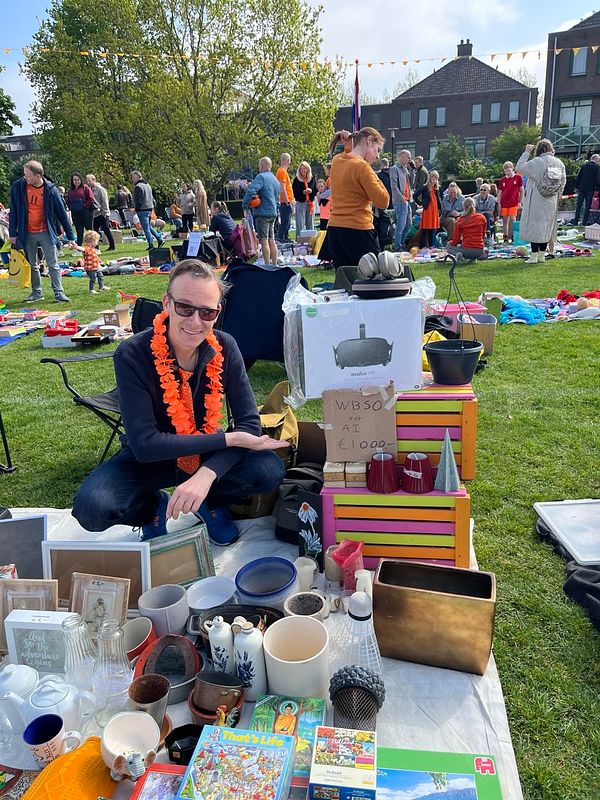A vendor is selling various items at a market during Kings Day, showcasing a sign for their business.