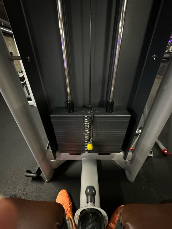 The image captures a view of a gym machine with weights and a person's feet in orange shoes.
