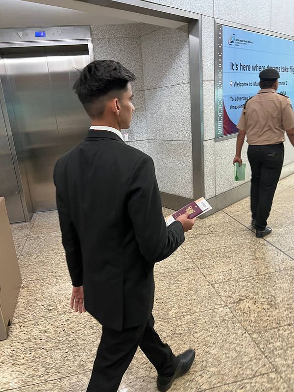A young man in a suit is walking through an airport terminal holding a document.