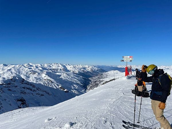 A group of skiers stands at the peak of a snowy mountain, enjoying a clear blue sky and breathtaking views.