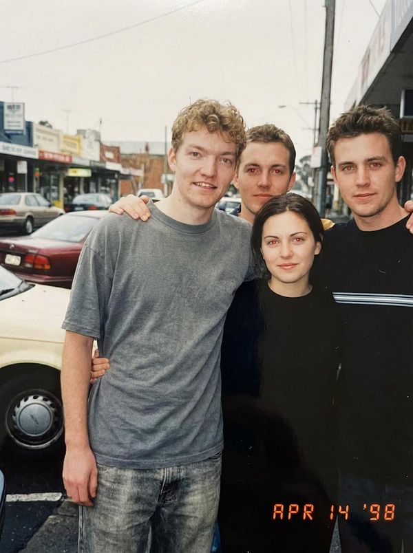 A group of four young adults poses together outdoors in a casual setting.