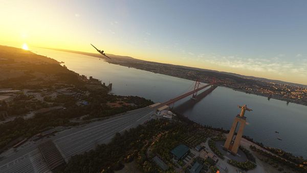 A scenic aerial view of a river at sunset, featuring a bridge and a prominent statue.