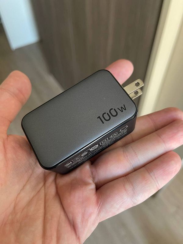 A hand holds a compact 100W laptop charger.