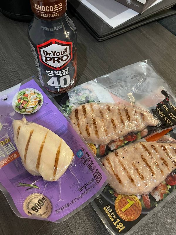 The image features a protein drink alongside packaged grilled chicken and a salad.