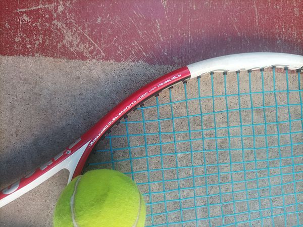 A tennis racket and a tennis ball are positioned on a textured surface.