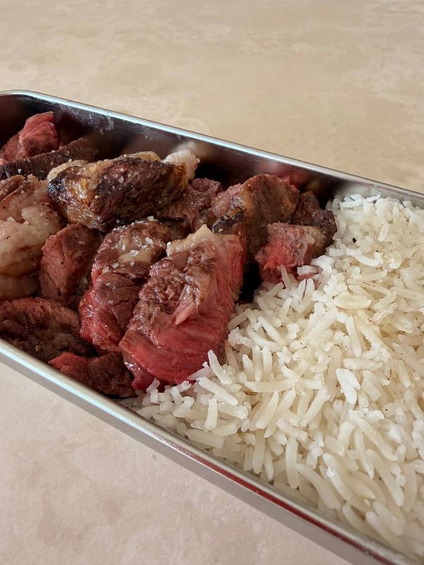 A meal tray with steak, rice, and fruit, presented on an airplane tray table.