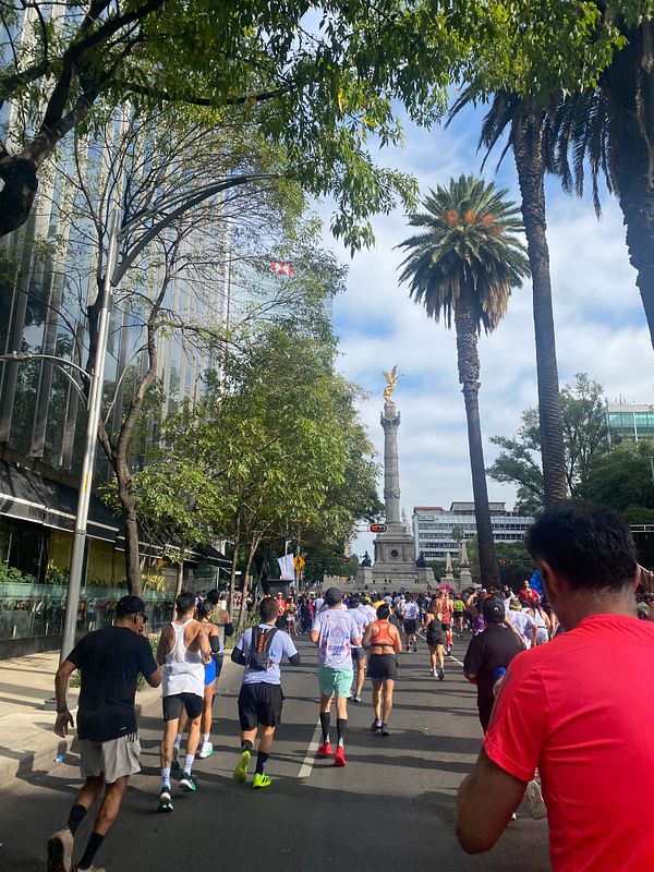 Runners participate in the Mexico City marathon, passing by a prominent monument amidst urban scenery.