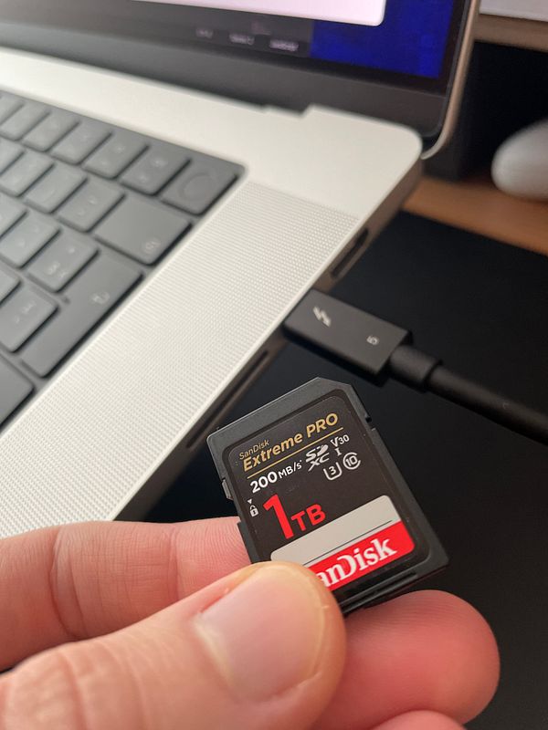 A hand holds a SanDisk Extreme PRO SD card next to a laptop.