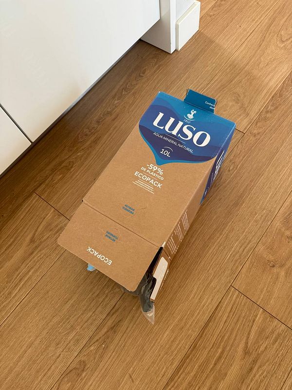 A 10L cardboard box of Luso mineral water is lying on a wooden floor.