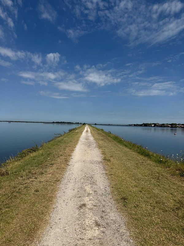 A narrow path stretches between calm waters under a clear blue sky.