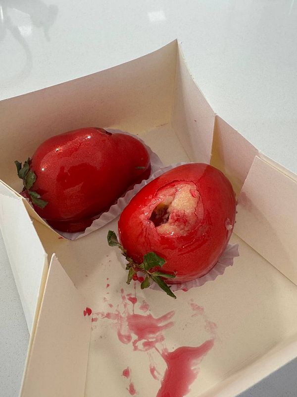Two unusual strawberries are presented in a takeout box, with one showing a bite taken out of it.