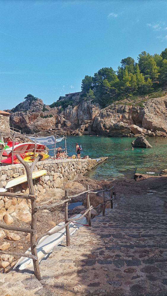 A scenic coastal area with rocky cliffs, clear water, and people enjoying the beach.