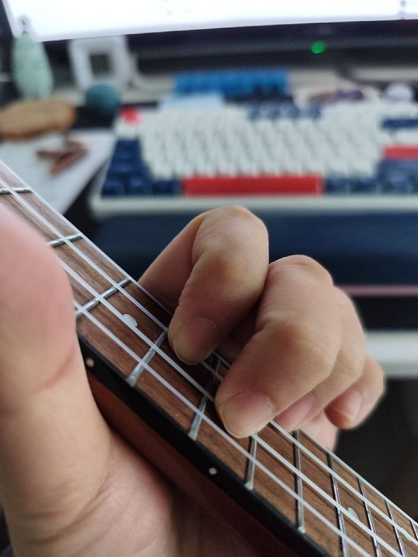 A close-up of a hand playing a ukulele with a blurred background.