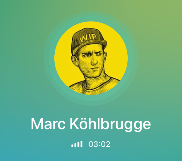 A man standing on rocks in the ocean at sunset, holding a camera tripod and wearing a long coat and a hat.